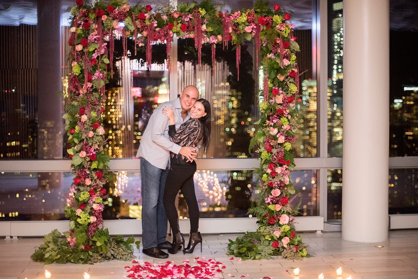 NYC Proposal Photos by Mikkel Paige Photography.  Cascading floral arch by The Arrangement NYC at Trump Soho overlooking Manhattan skyline. 