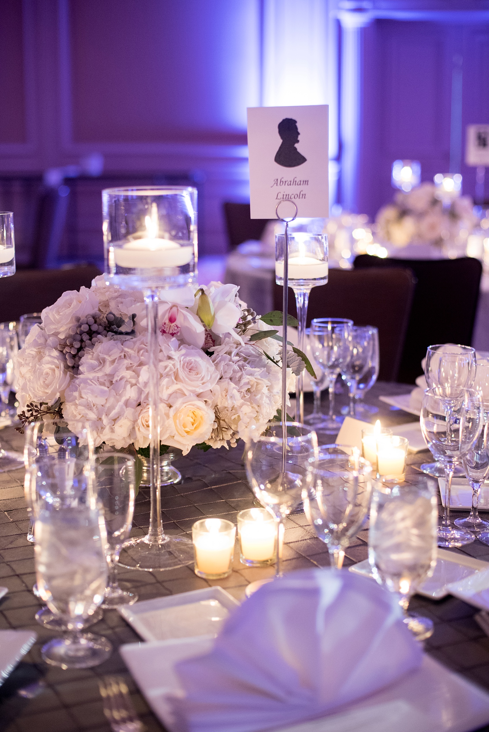 Washington, DC wedding photos by Mikkel Paige. The main ballroom with purple lighting and white flowers, with president name table numbers at the Ritz Carlton, Pentagon City.