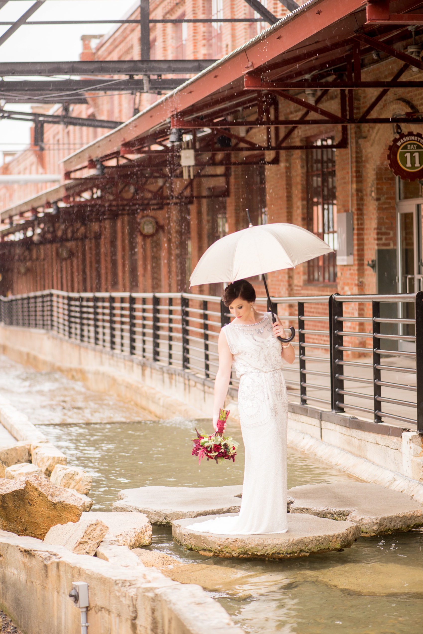Bay 7 wedding photos by Mikkel Paige Photography. Raleigh wedding photographer captures the bride in her art deco gown in the rain with an umbrella.