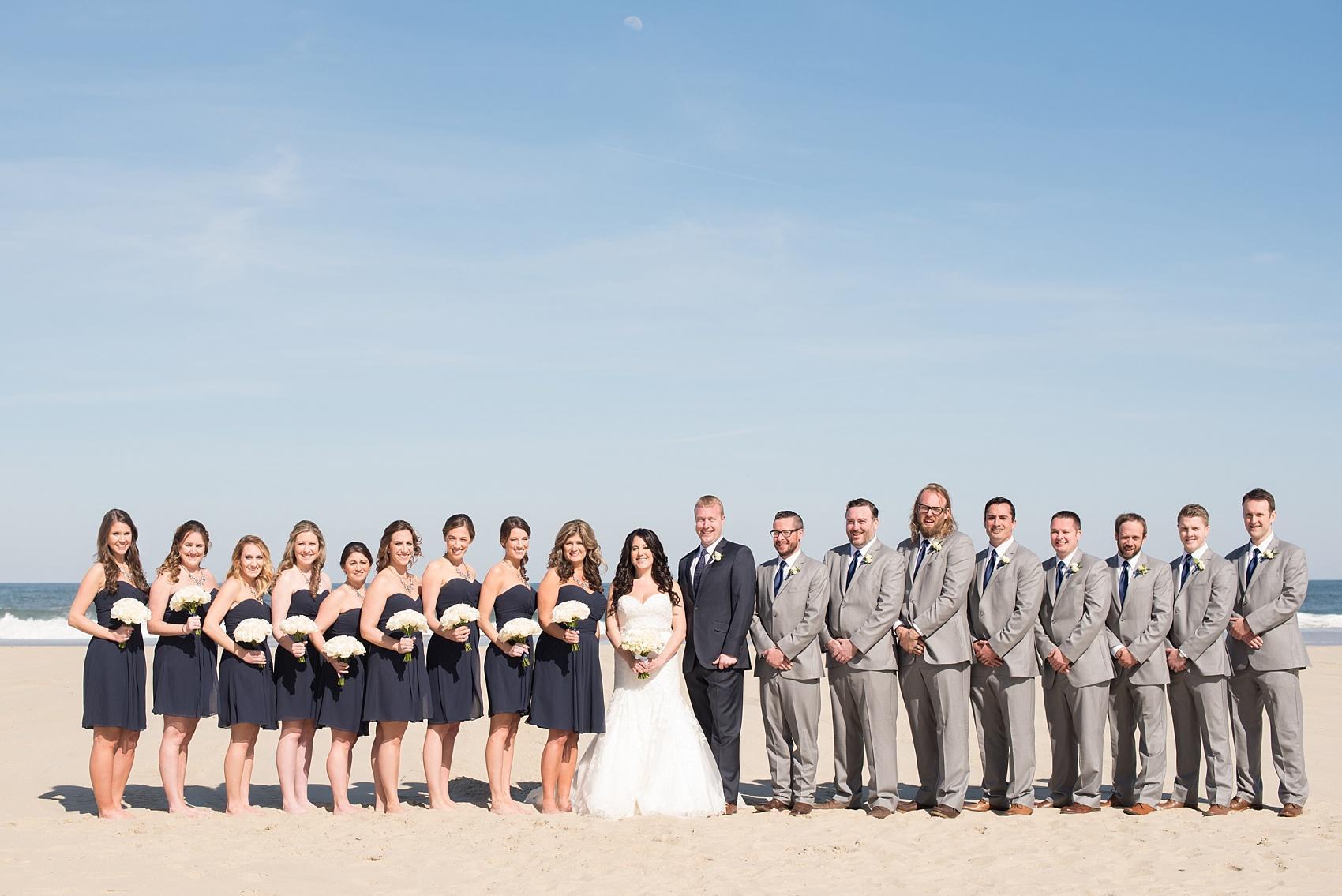 Photo by Mikkel Paige photography. Bridesmaids in navy chiffon short dresses with white rose bouquets. The groomsmen in grey suits and groom in a navy suit.
