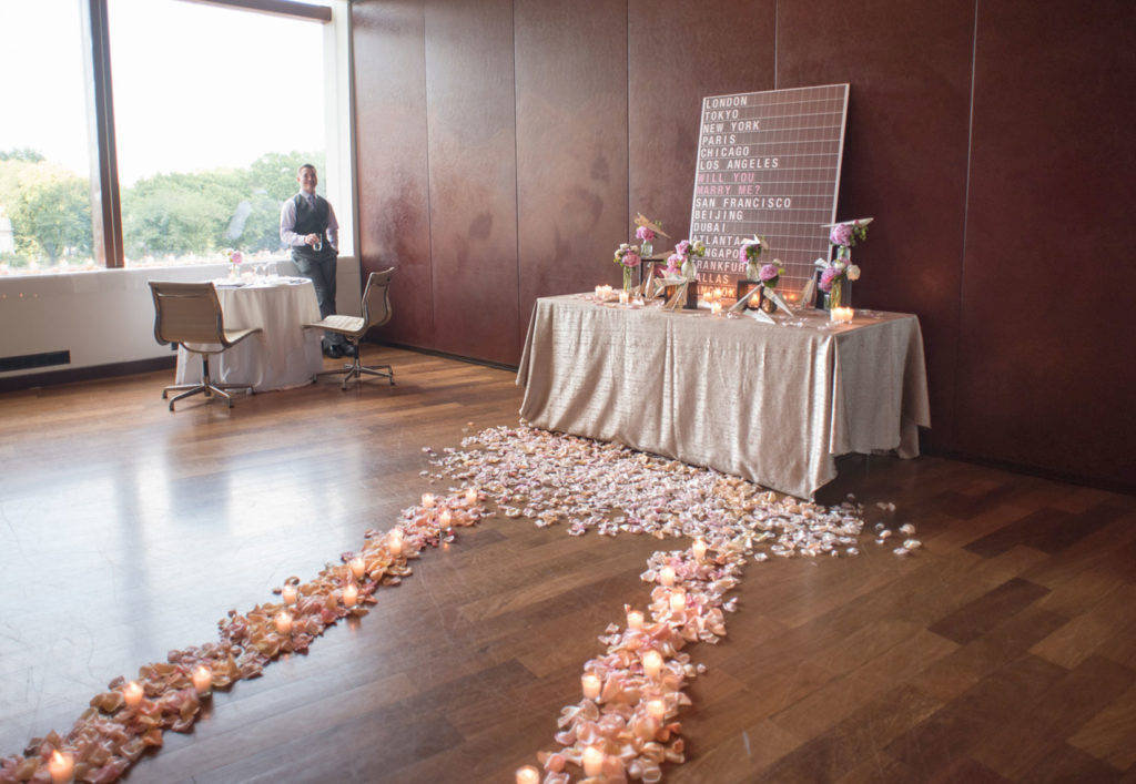 NYC Proposal Photographer Mikkel Paige Photography captures a travel themed marriage proposal in Columbus Circle with calligraphy on paper airplanes, rose petals and candles on the floor.