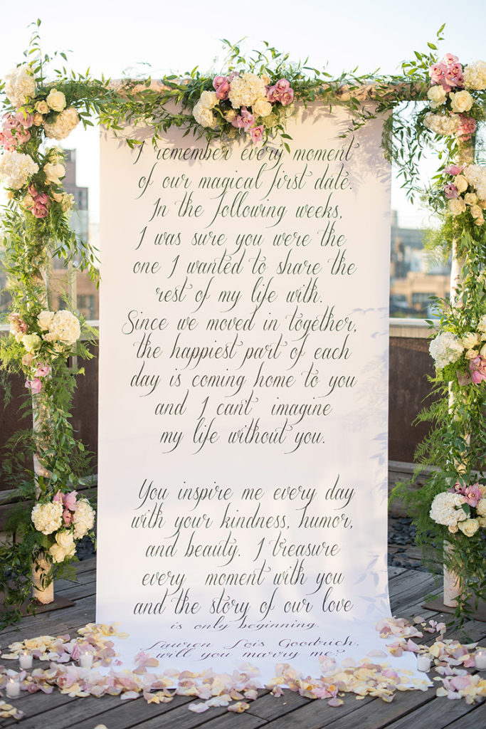 NYC rooftop proposal photos by Mikkel Paige Photography, New York wedding photographer. Custom calligraphy backdrop and floral arch.