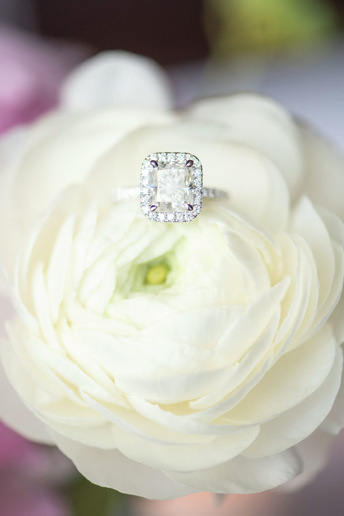 NYC Proposal Photographer Mikkel Paige Photography captures a travel themed marriage proposal in Columbus Circle with a rectangle diamond engagement ring and white ranunculus flowers.
