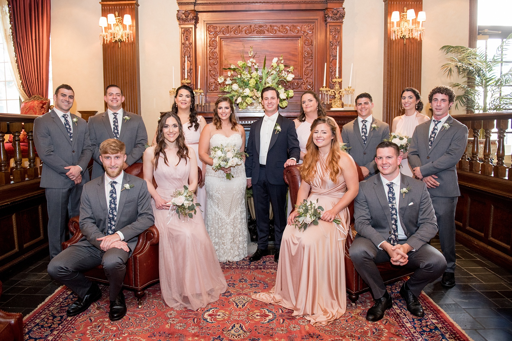 Mikkel Paige Photography photo of a wedding at Madison Hotel in NJ with the bridal party in light pink mismatched dresses. Entire wedding party near the fireplace in a Vogue style.