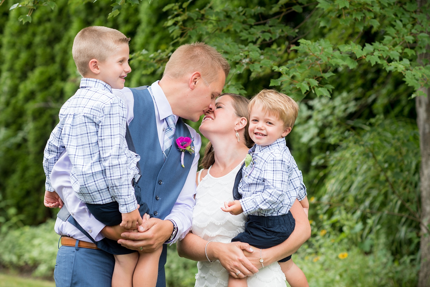 Mikkel Paige Photography photo of an anniversary session with the bride and groom in a short white dress and blue suit, with their sons as ring bearers in plaid shirts and navy ties.