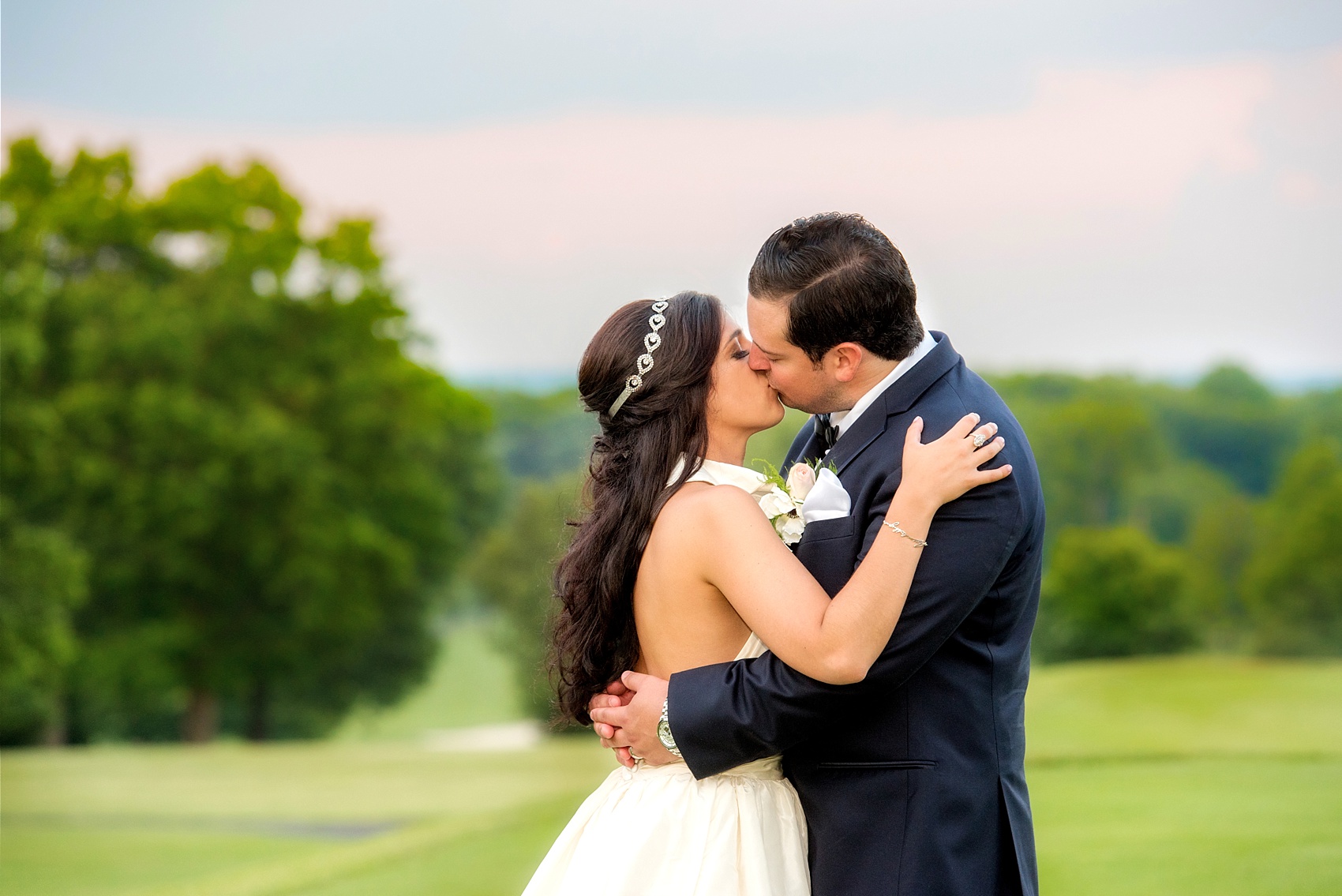Mikkel Paige Photography photos from a wedding at Basking Ridge Country Club, NJ. The bride in a halter Amsale gown and groom in a navy blue suit kiss at a picturesque pink and blue sunset.