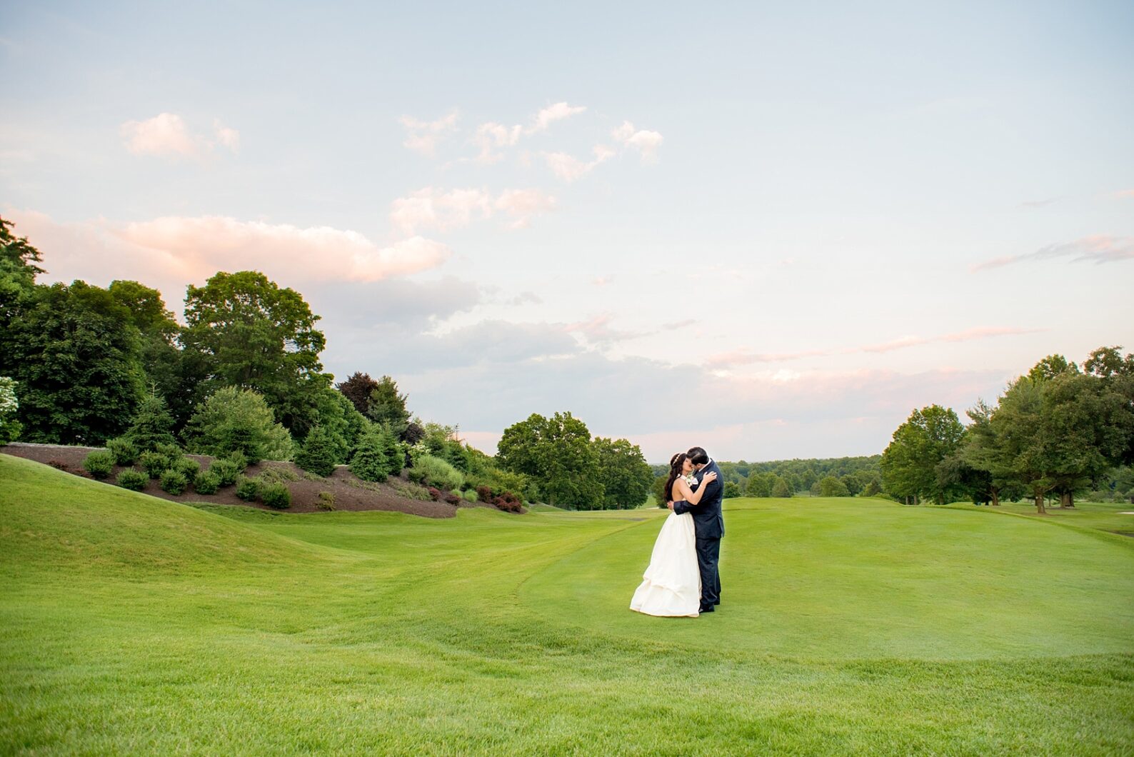 Mikkel Paige Photography photos from a wedding at Basking Ridge Country Club, NJ. The bride in a halter Amsale gown and groom in a navy blue suit kiss at a picturesque pink and blue sunset on the golf course.