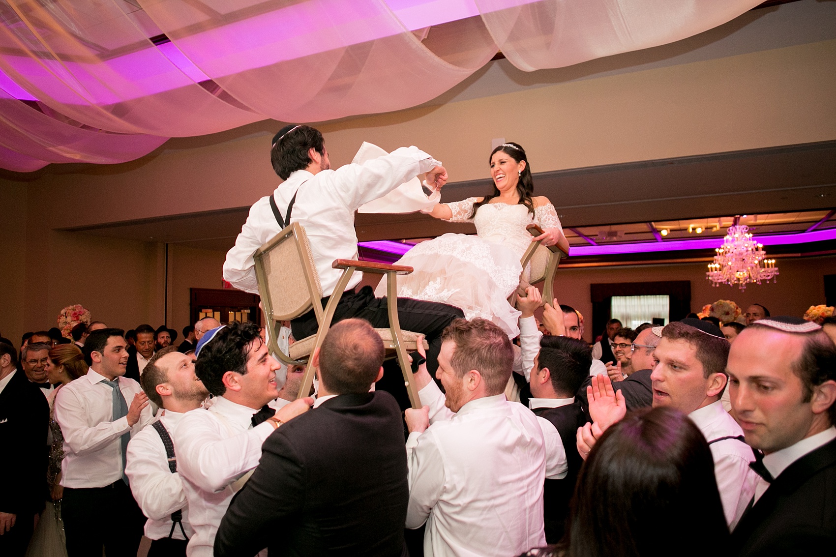 Mikkel Paige Photography photos of an elegant reception with pink and white details at Temple Emanu-El in Closter, NJ. The couple dances to the hora and is lifted in chairs! 