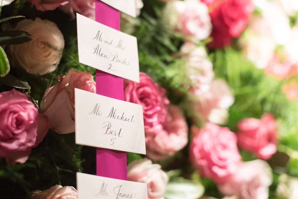 Mikkel Paige Photography wedding photos at The Glasshouses NYC. A flower wall escort card presentation with pink ribbon and calligraphy.