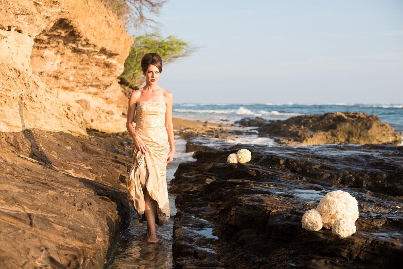 Mikkel Paige Photography photos of a bridal session on beach in Oahu. Golden hour bride with beehive up do and metallic gown. Rose pomanders filled the lava rock shore.
