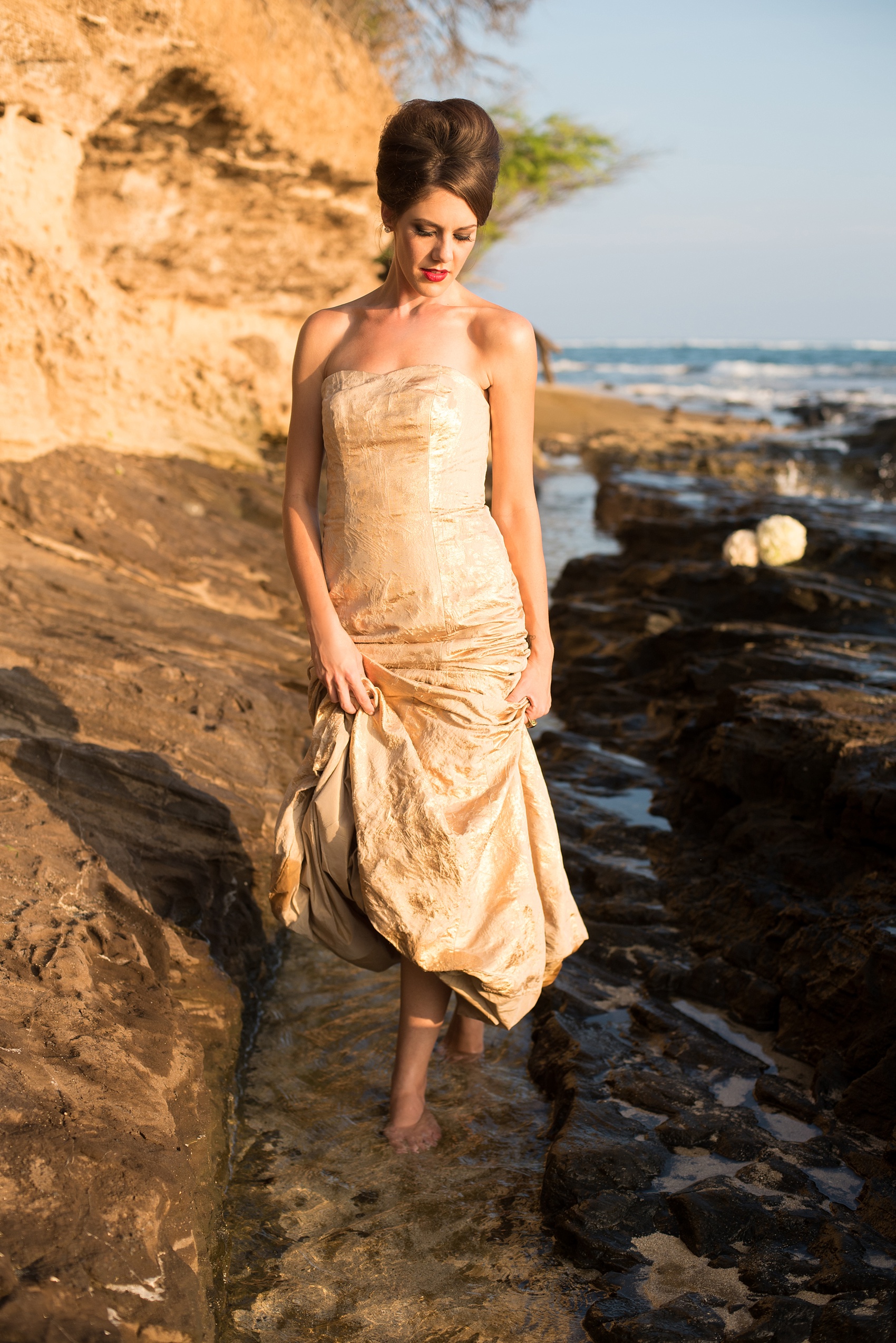 Mikkel Paige Photography photos of a bridal session on beach in Oahu. Golden hour bride with beehive up do and metallic gown. Rose pomanders filled the lava rock shore.
