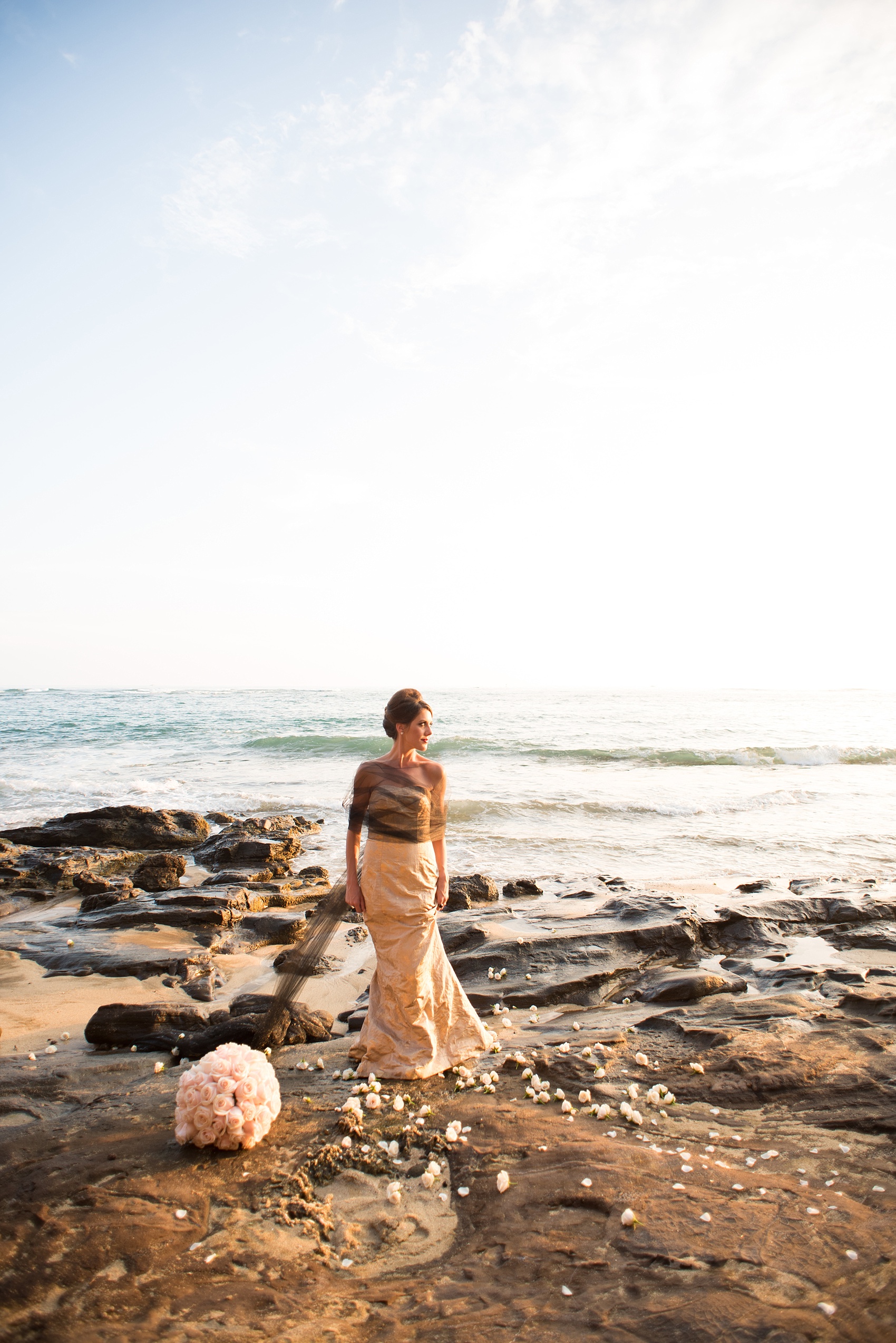 Mikkel Paige Photography photos of a bridal session on beach in Oahu. Golden hour bride with beehive up do, metallic gown and rose pomanders on the lava rock shore.