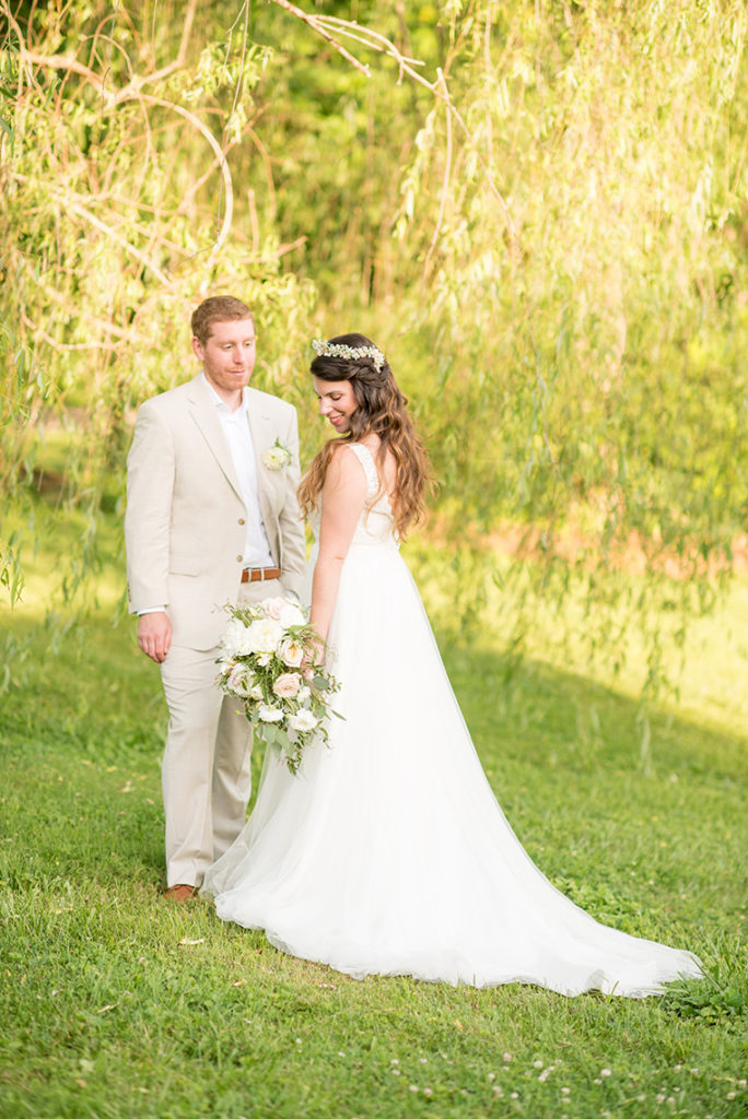 Mikkel Paige Photography photo of a rustic chic farm wedding at Spring Hill Manor, Maryland. Outdoor images of the bride and groom by a Weeping Willow tree with the bride in a lace, v-neck gown and groom in a tan linen suit.