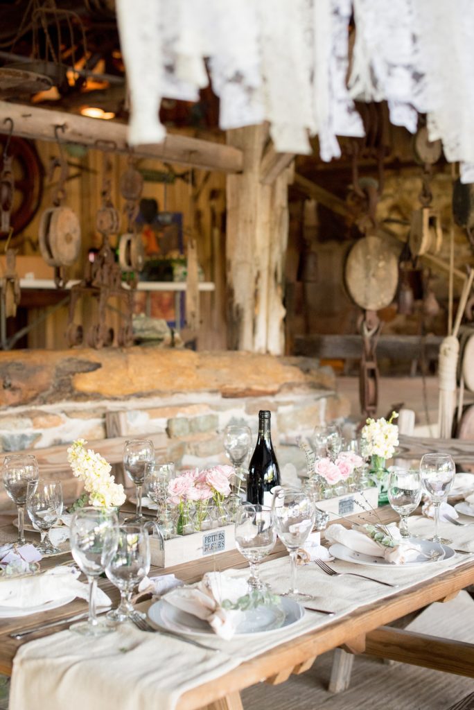 Mikkel Paige Photography photos of a wedding at Spring Hill Manor in Maryland. Image of rustic farm tables with single bud vases with snapdragon and peony flowers and lace garland strands.