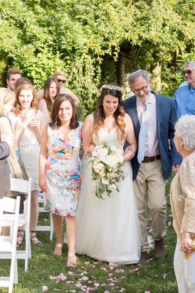 Mikkel Paige Photography photos of a wedding at Spring Hill Manor in Maryland. Image of the bride walking down the outdoor ceremony aisle with her parents and cascading bouquet.