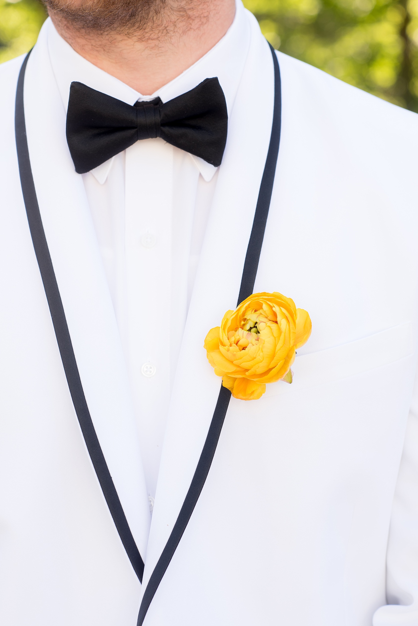 Mikkel Paige Photography wedding photo at The Bradford, NC. Groom in a white tuxedo suite jacket with black edge detail and a yellow ranunculus boutonniere alternative.