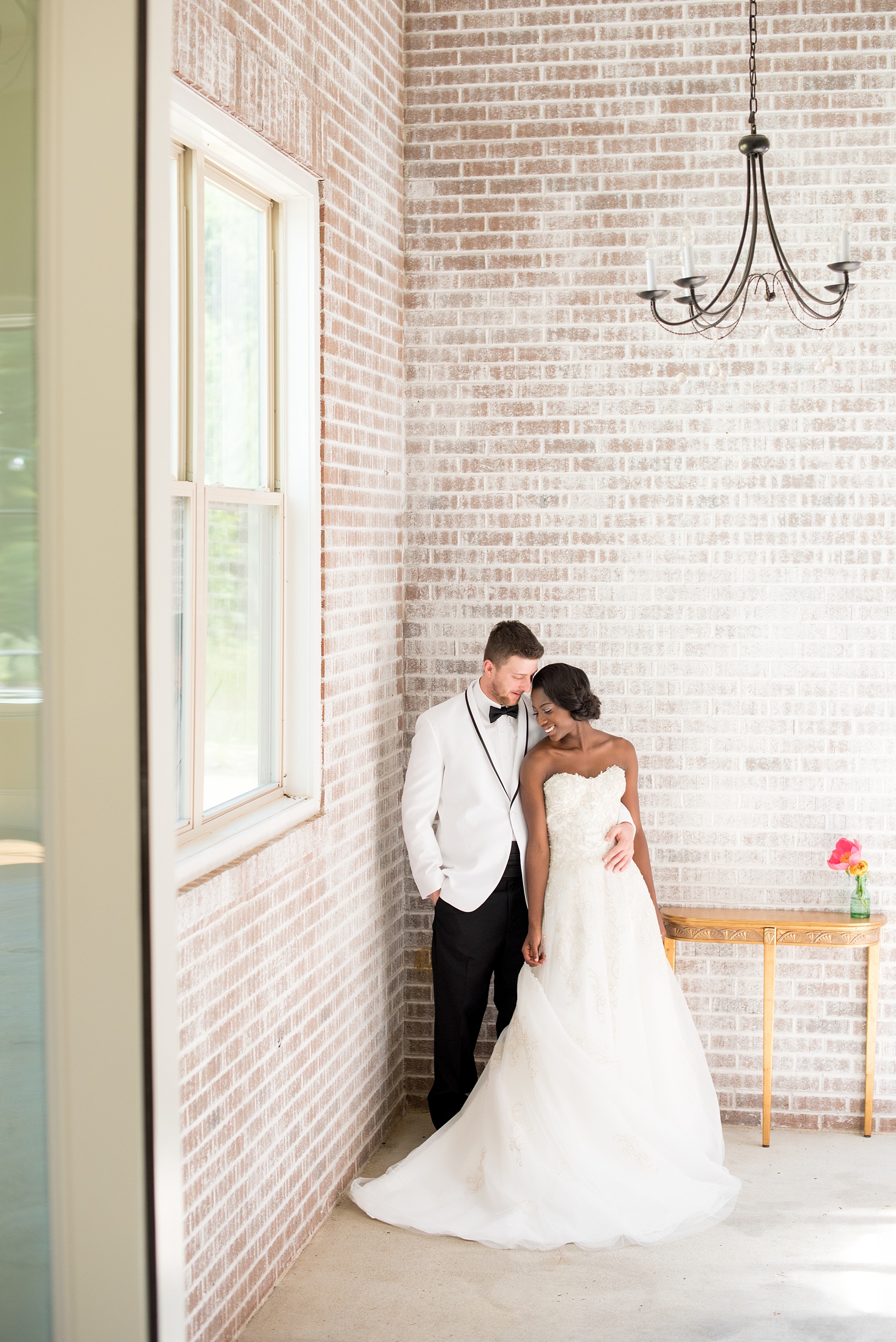 Mikkel Paige Photography photo at The Bradford, NC. Bride and groom of mixed race against the elegant NC home's white brick wall.