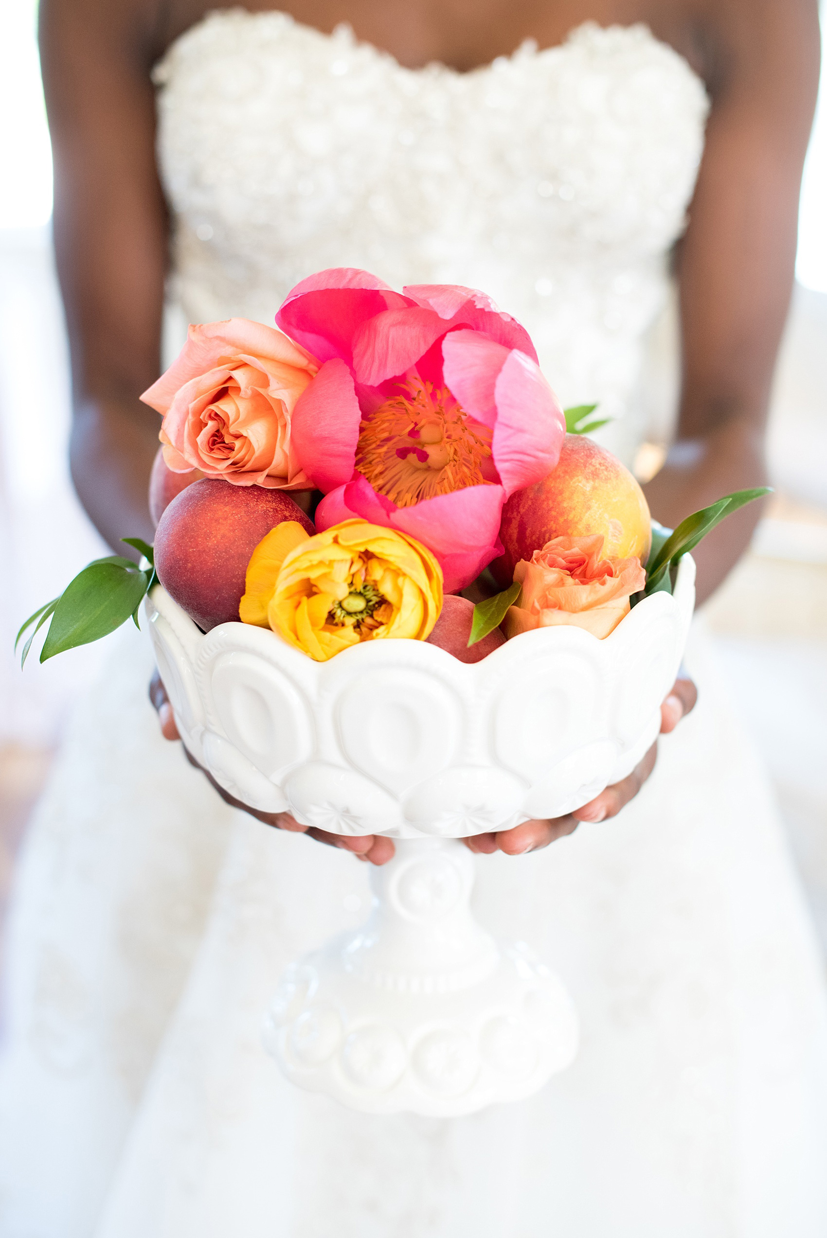 Mikkel Paige Photography photo at The Bradford, NC. Bride holding a milk glass vase full of pink peonies, yellow ranunculus and peaches.