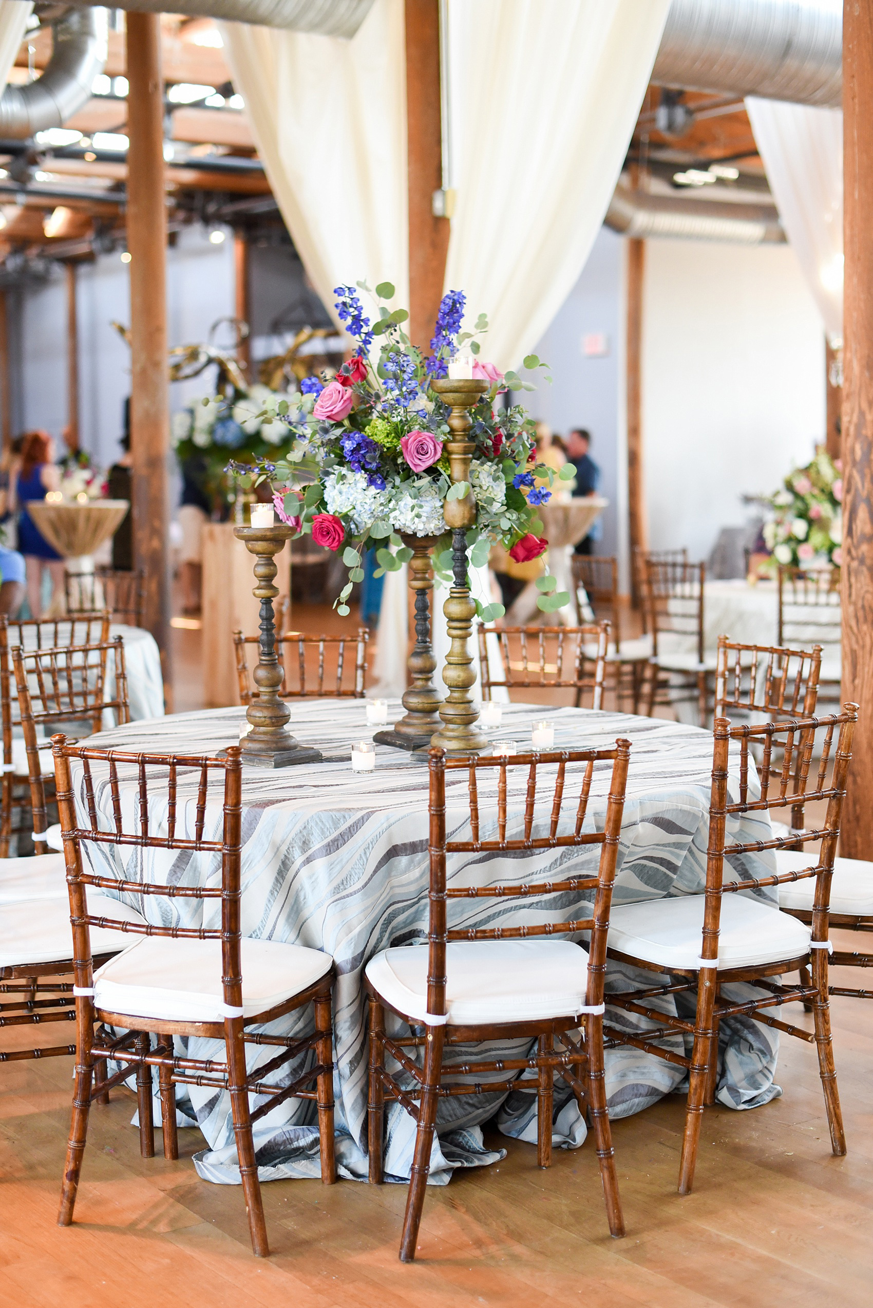 Mikkel Paige Photography photos from The Cotton Room wedding venue in Durham, NC. Wavy blue linens complete with candlelight and high floral arrangements.