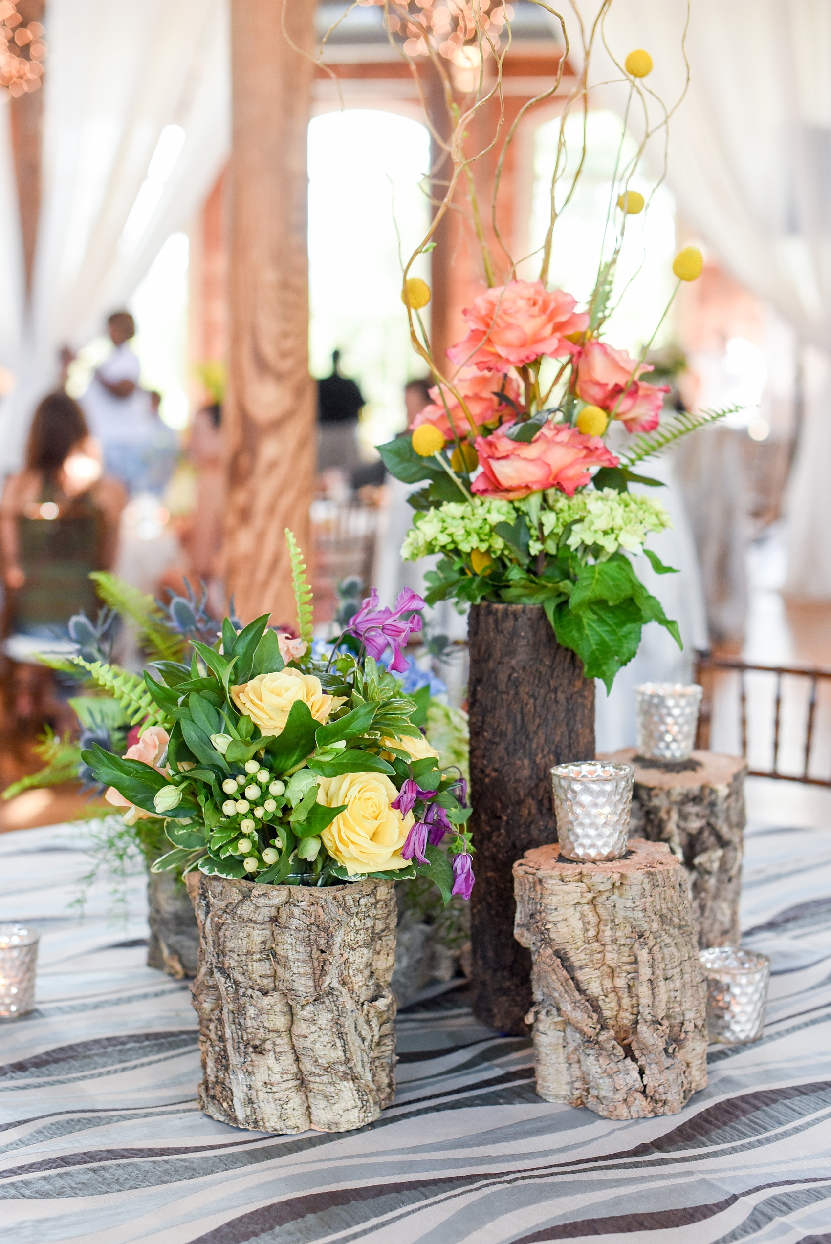 Mikkel Paige Photography photos from The Cotton Room wedding venue in Durham, NC. Wavy blue linens complete with floral centerpiece arrangements with rustic wooden tree trunk containers.