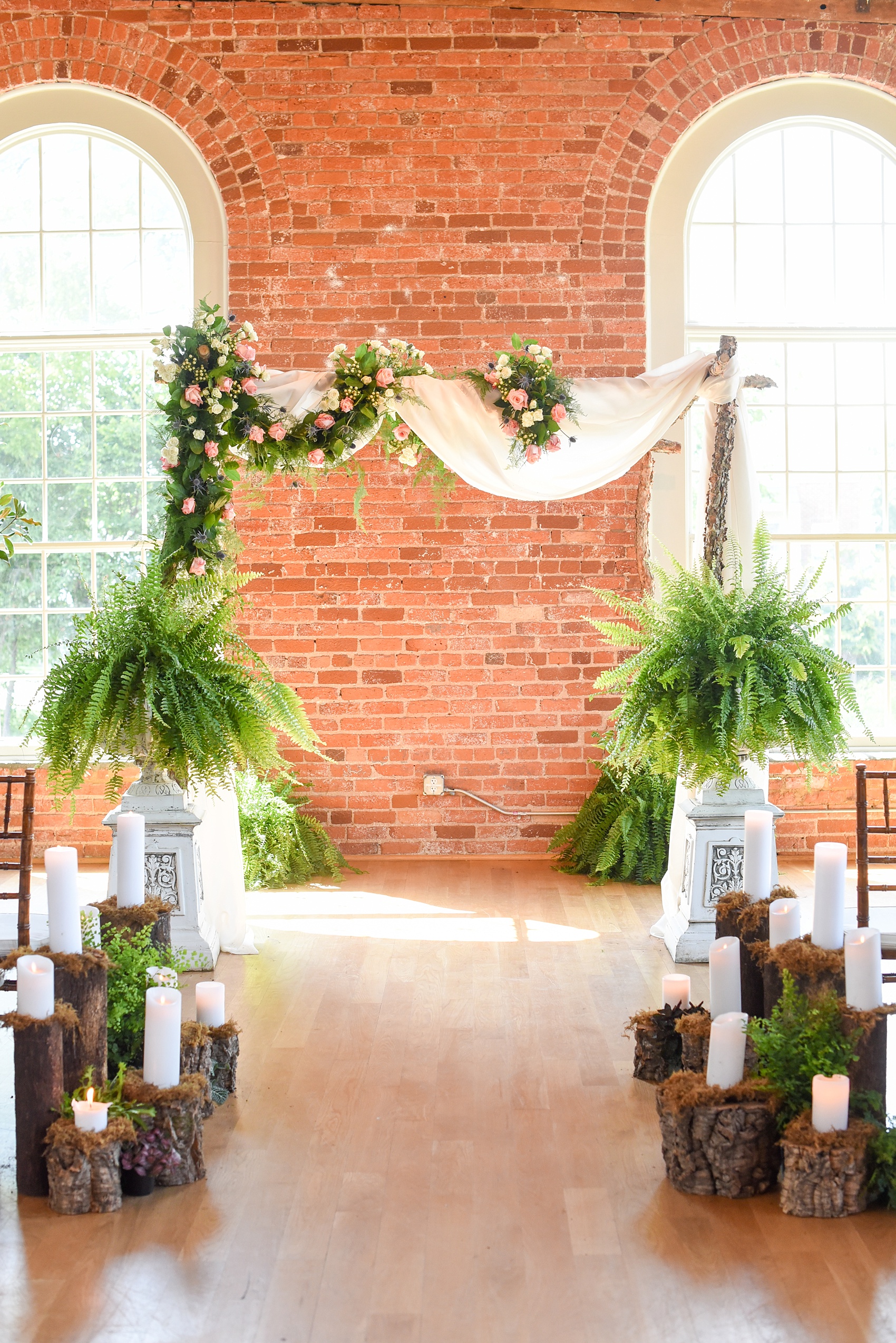 Mikkel Paige Photography image from The Cotton Room wedding venue in Durham, NC. A wooden fairy forest scene of candles and wood tree trunk stumps with moss lined the ceremony aisle.