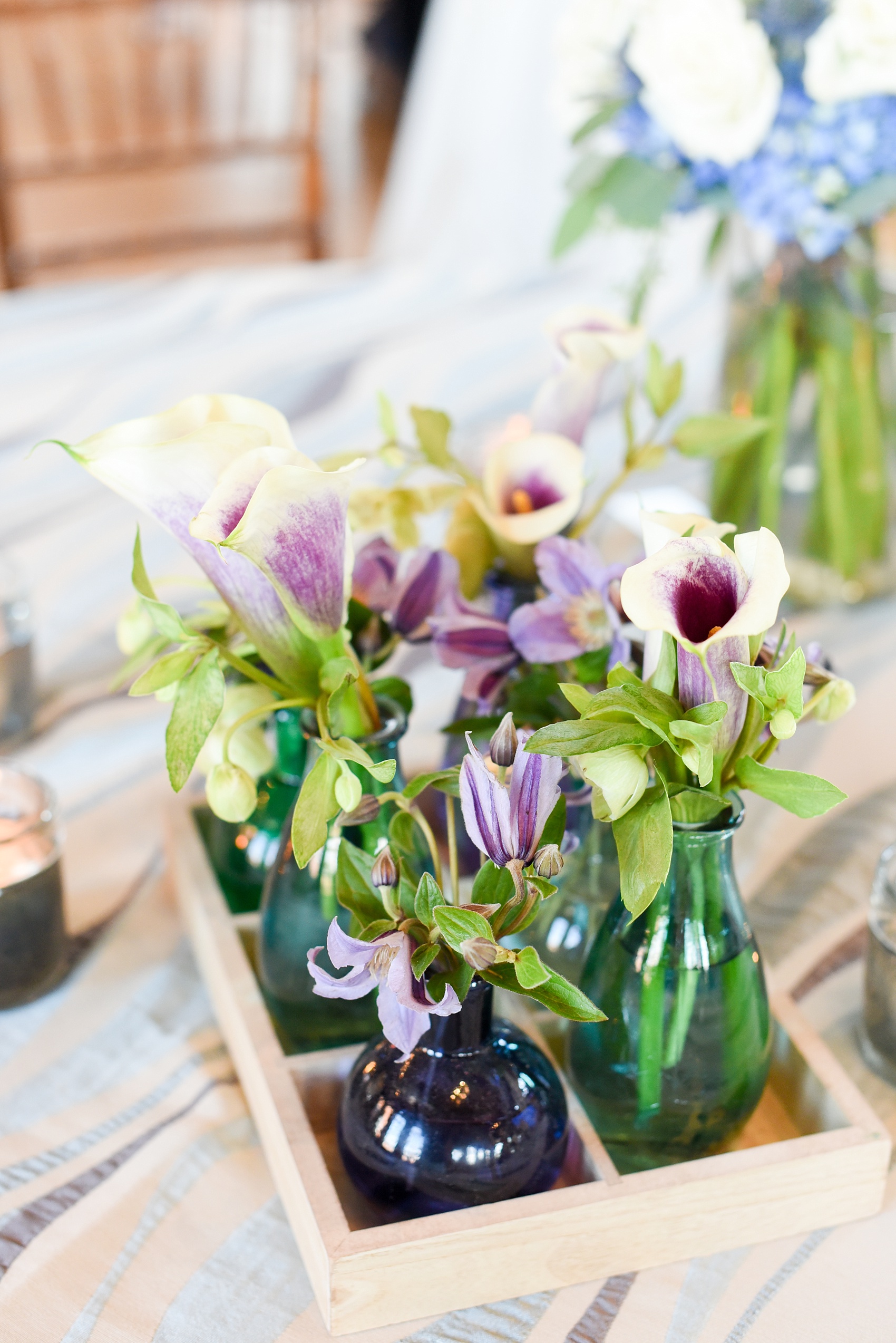 Mikkel Paige Photography image from The Cotton Room wedding venue in Durham, NC. Fresh flowers in bud vases of varying blue shades sat in a rustic wooden tray container. Picasso calla lilies and helleborus flowers completed the look.