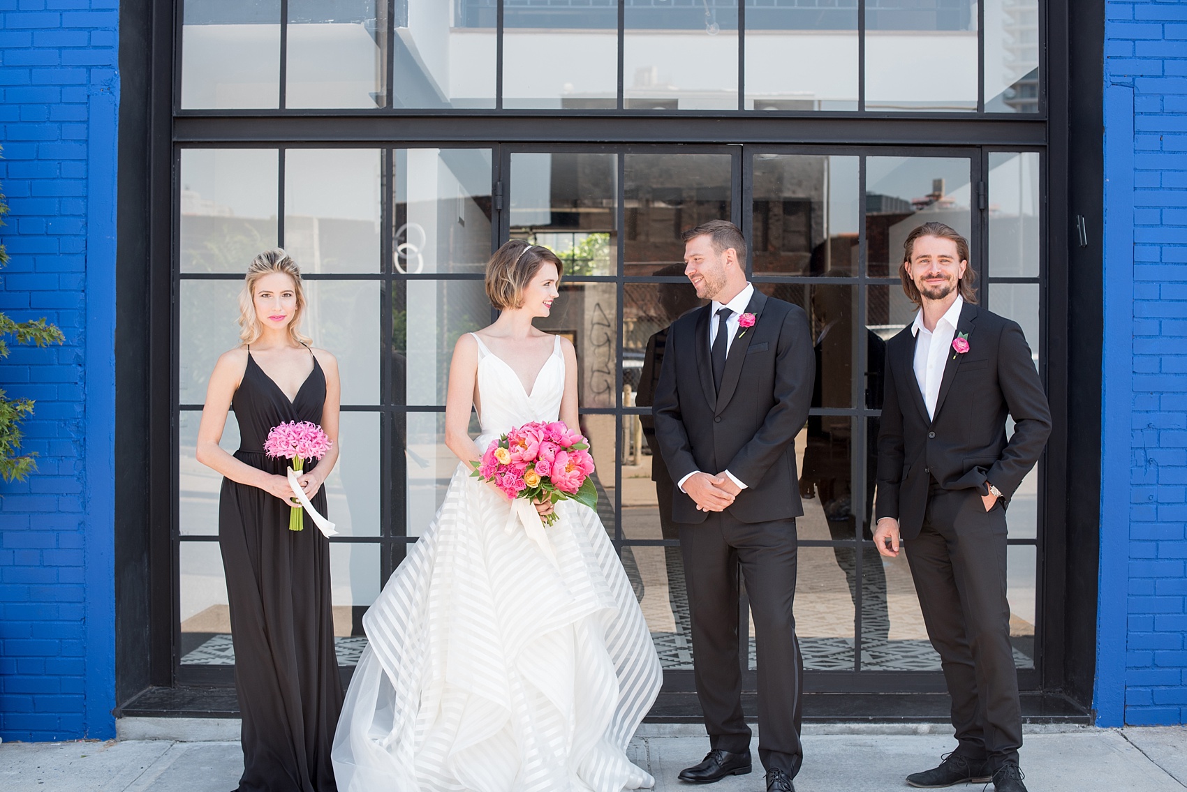 Mikkel Paige Photography photo of Dobbin St Brooklyn wedding. Planning and coordination by Color Pop Events. Classic wedding party in black and white against a colorful blue wall. Bride in Hayley Paige white striped gown with short hair do with headband detail. Peony and ranunculus bouquet by Blade NYC.