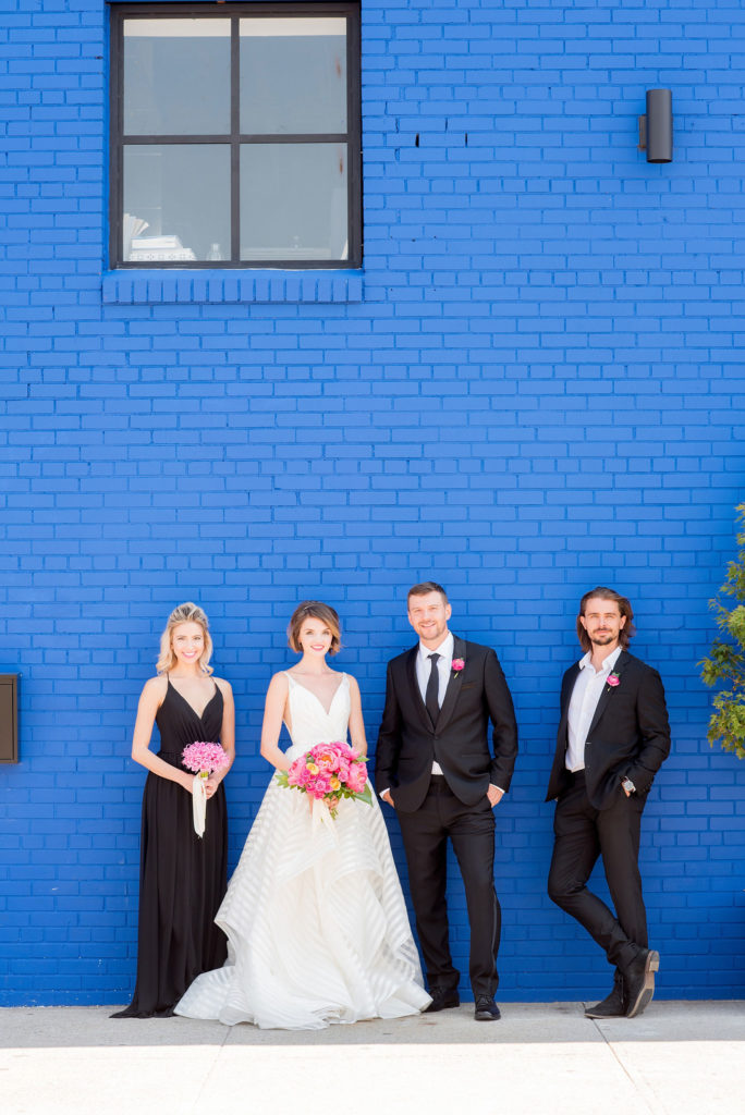 Mikkel Paige Photography photo of Dobbin St Brooklyn wedding. Planning and coordination by Color Pop Events. Classic wedding party in black and white against a colorful blue wall. Bride in Hayley Paige white striped gown with short hair do with headband detail. Peony and ranunculus bouquet by Blade NYC.