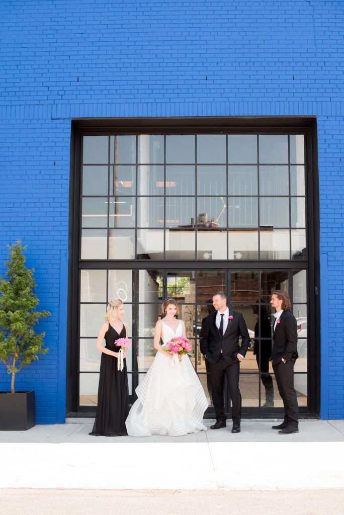 Mikkel Paige Photography photo of Dobbin St Brooklyn wedding. Planning and coordination by Color Pop Events. Classic wedding party in black and white against a colorful blue wall. Bride in Hayley Paige white striped gown with short hair do with headband detail. Peony and ranunculus bouquet by Blade NYC.
