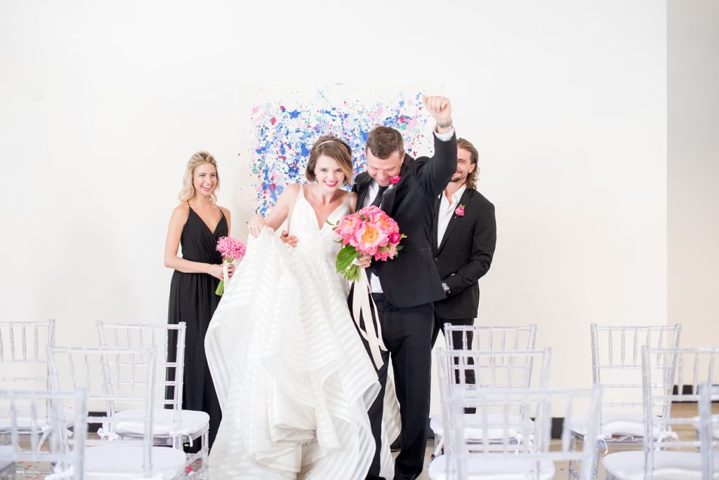 Mikkel Paige Photography photo of Dobbin St Brooklyn wedding. Planning and coordination by Color Pop Events. Ceremony confetti toss with clear chiavari chairs and custom art splatter paint backdrop for the bride and groom's first kiss.