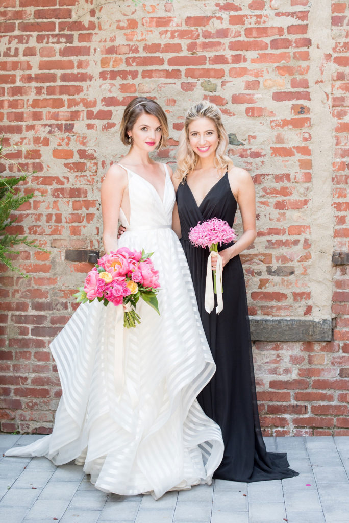 Mikkel Paige Photography photo of Dobbin St Brooklyn wedding. Planning and coordination by Color Pop Events. Bride in a white striped Hayley Paige gown and bridesmaid in a classic occasions chiffon gown. Outdoor patio image against greenery and rustic brick.