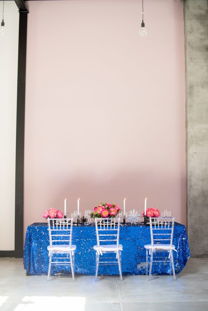 Mikkel Paige Photography photo of Dobbin St Brooklyn wedding. Planning and coordination by Color Pop Events. Reception table with blue sequins, pink peony centerpieces and clear chiavari chairs against a mauve wall.