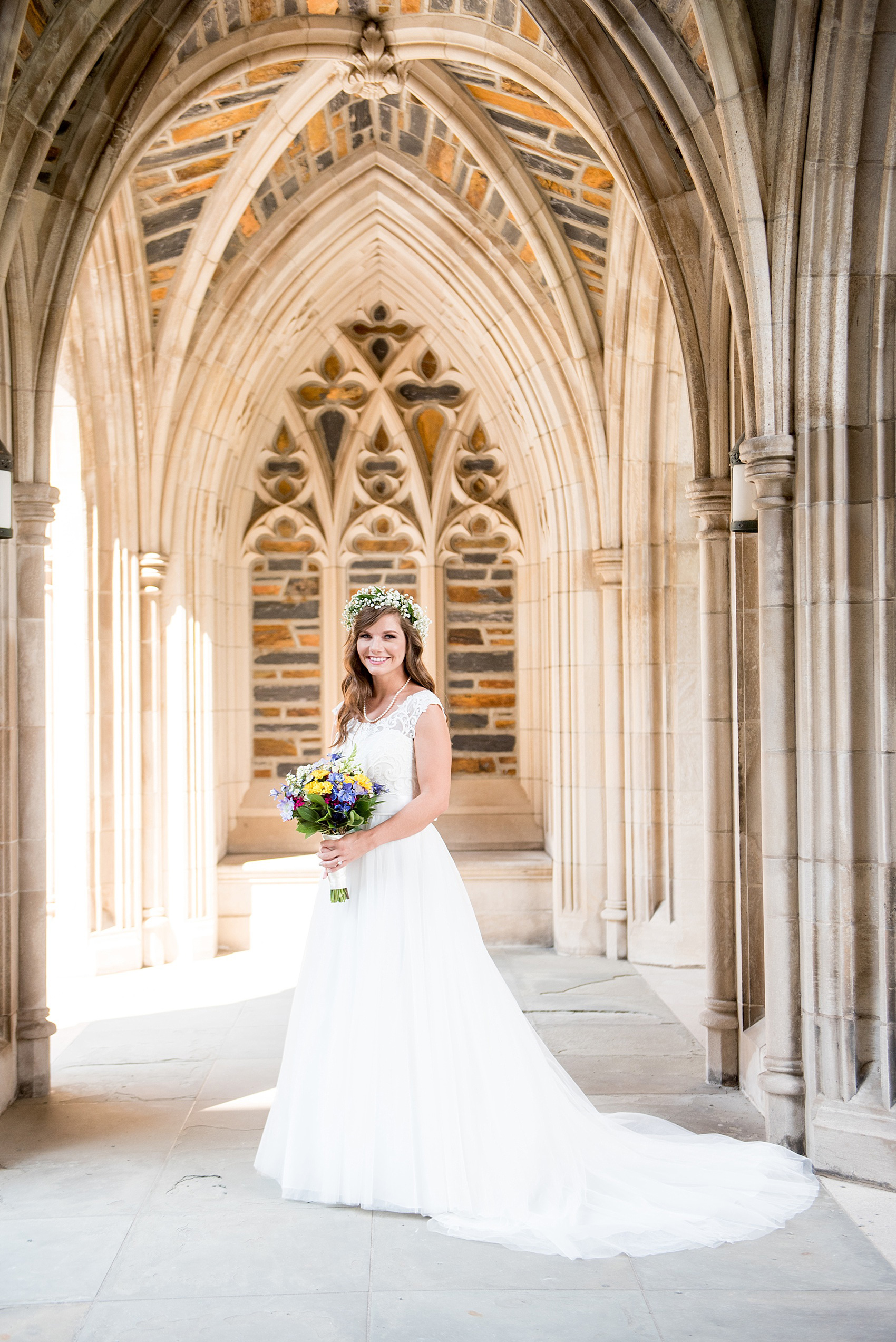 Mikkel Paige Photography photo of a Duke Chapel wedding in Durham, North Carolina. The bride in a lace cap sleeve gown with a wildflower bouquet and Baby's Breath floral crown under the gothic arches of the iconic church.