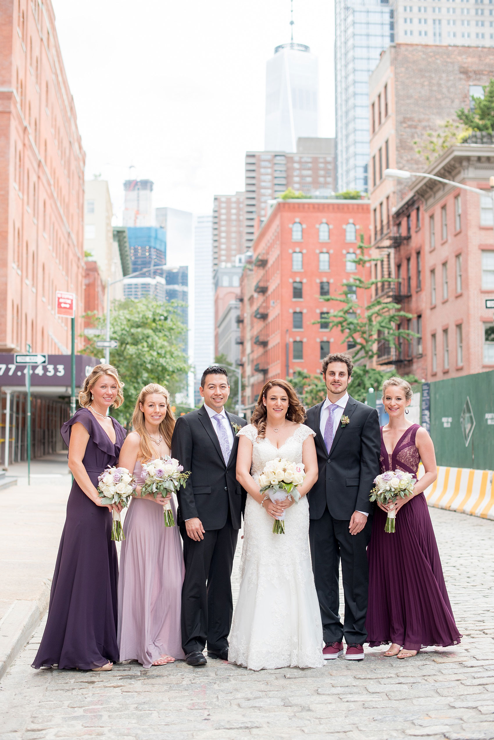 Mikkel Paige Photography photos of a NYC wedding at Tribeca Rooftop. An urban image of the wedding party in shades of mismatched purple dresses with rose and succulent bouquets.