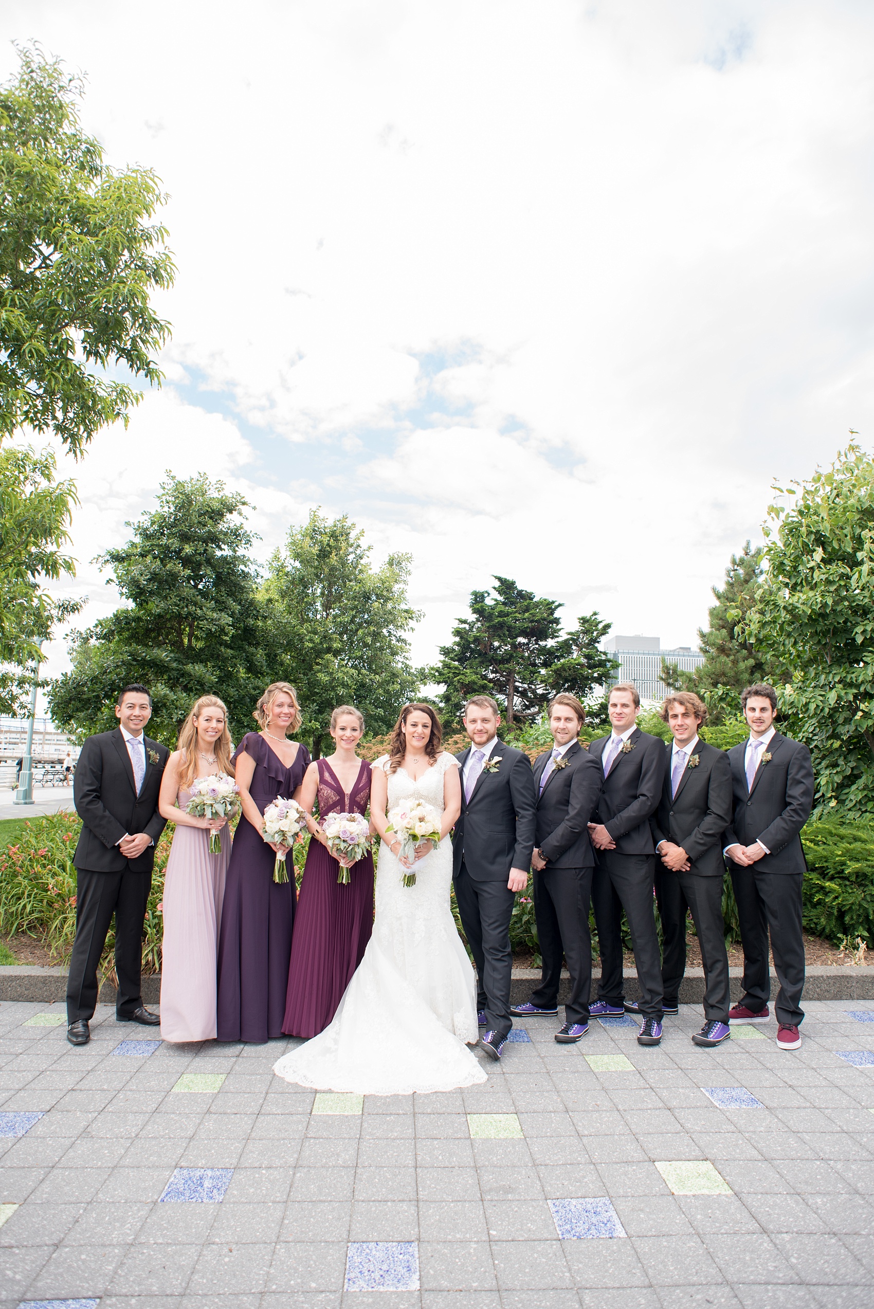 Mikkel Paige Photography photos of a NYC wedding at Tribeca Rooftop. An urban image of the wedding party in shades of mismatched purple dresses with rose and succulent bouquets and groomsmen in paisley purple ties and custom Converse sneakers.