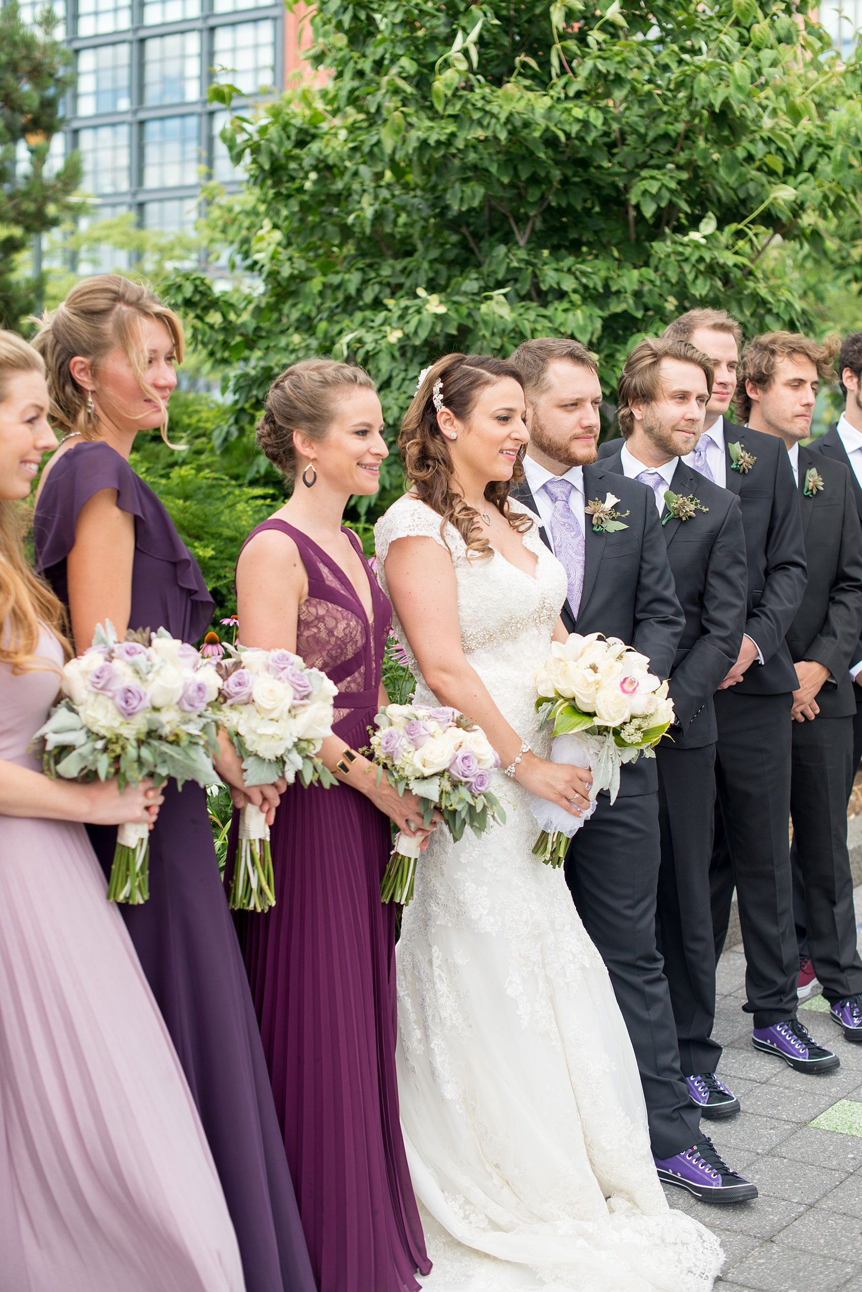 Mikkel Paige Photography photos of a NYC wedding at Tribeca Rooftop. An image of the wedding party/bridal party in mismatched purple dresses at Hudson River Park with rose bouquets.