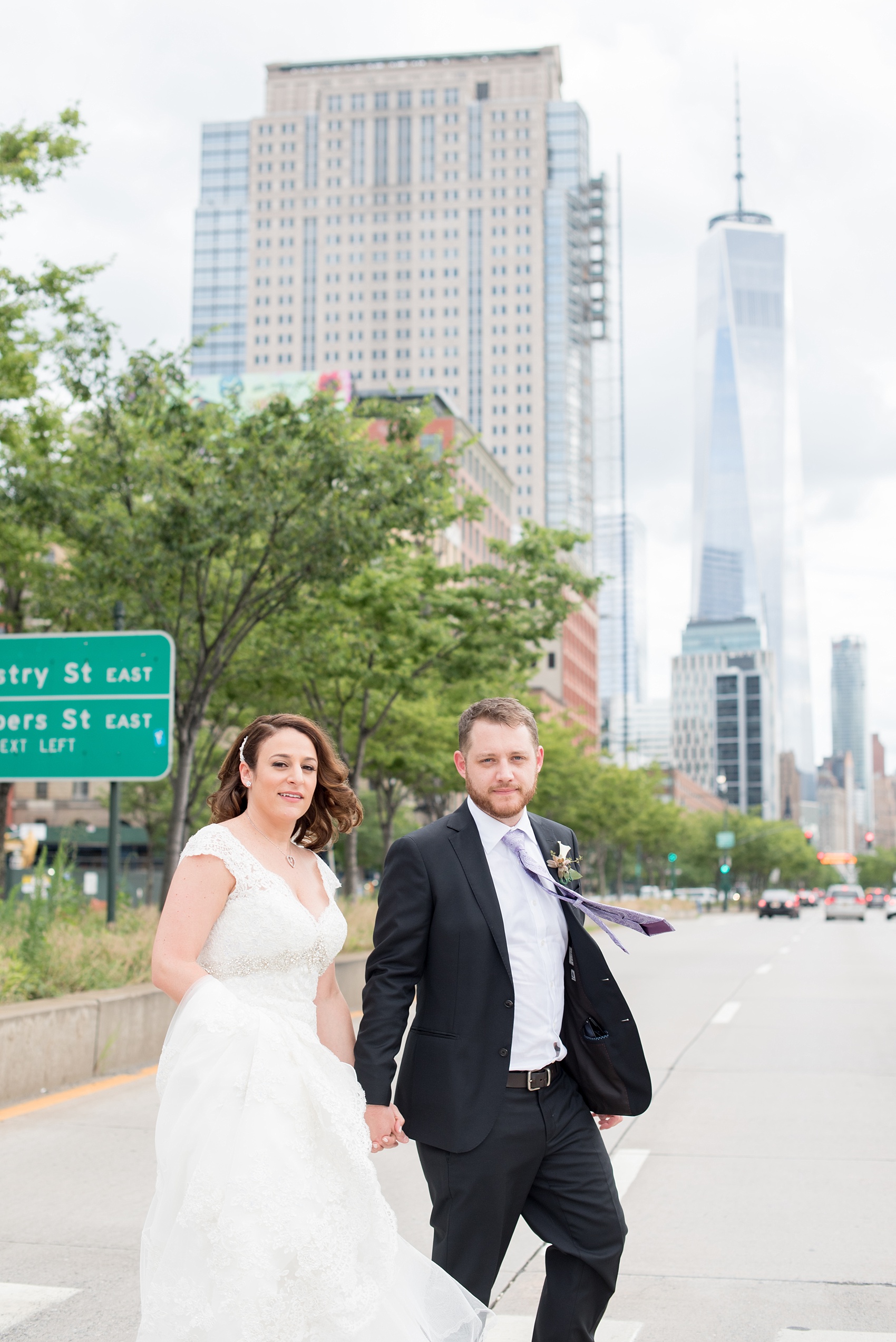 Mikkel Paige Photography photos of a NYC wedding at Tribeca Rooftop. An image of the bride and groom crossing West Side Highway with the Freedom Tower in the background in lower Manhattan.