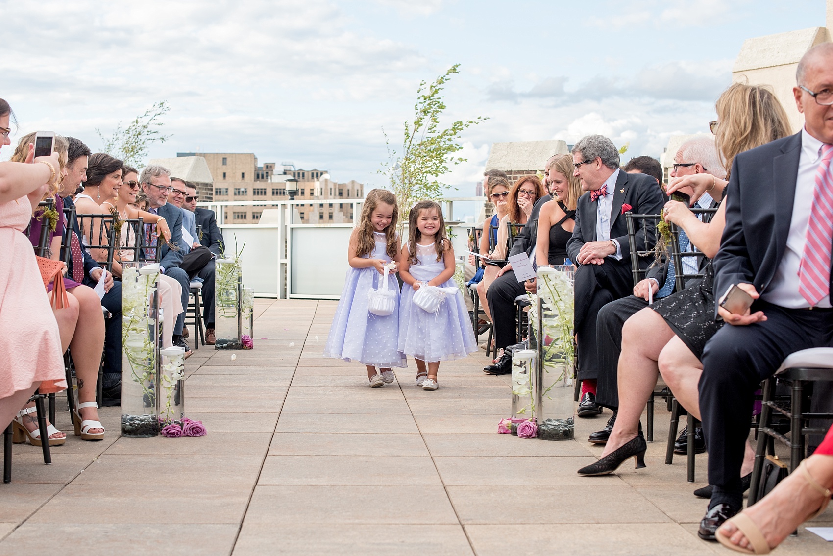 Mikkel Paige Photography photos of a NYC wedding at Tribeca Rooftop. An image of the flower girls in purple dresses walking down the aisle.