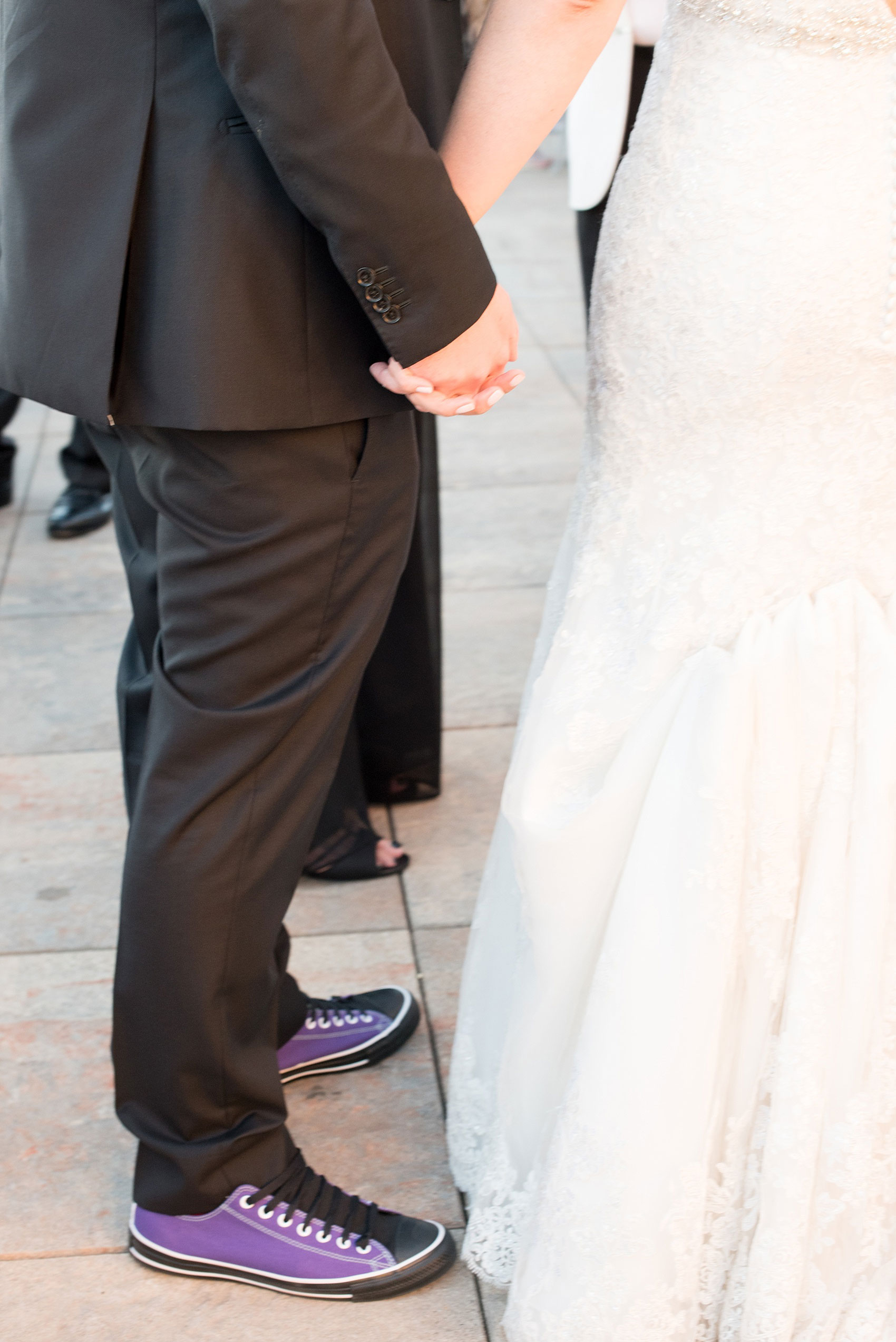 Mikkel Paige Photography photos of a NYC wedding at Tribeca Rooftop. An image of the bride and groom holding hands and his purple custom Converse sneakers.