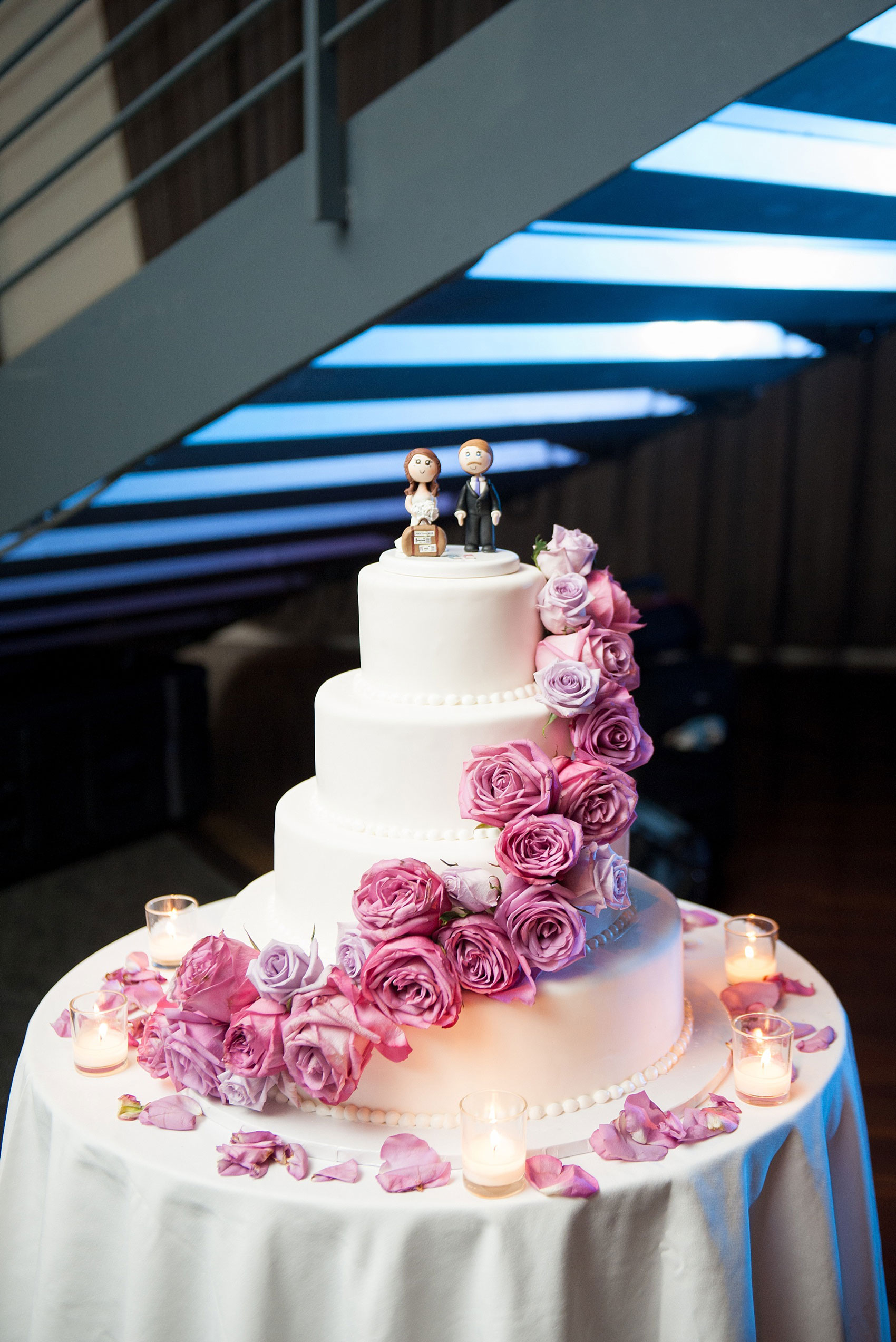 Mikkel Paige Photography photos of a NYC wedding at Tribeca Rooftop. Image of the white fondant, purple rose decorated cake with a clay topper of a traveling couple.