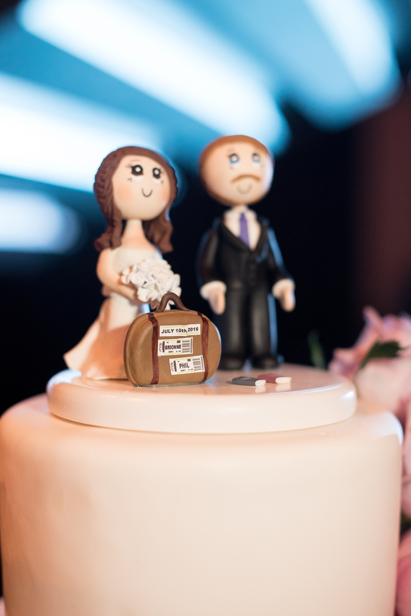 Mikkel Paige Photography photos of a NYC wedding at Tribeca Rooftop. Image of the white fondant, purple rose decorated cake with a clay topper of a traveling couple.