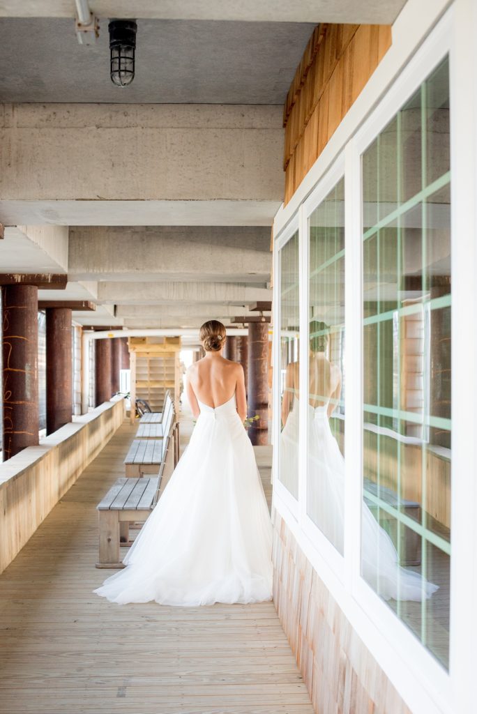 Mikkel Paige Photography photos of a Bay Head Yacht Club nautical wedding. The bride wore a low back sweetheart neckline gown from Kleinfeld and a low bun hari do. We caught her reflection in the window of this unique image as she walked towards the groom for their first look.