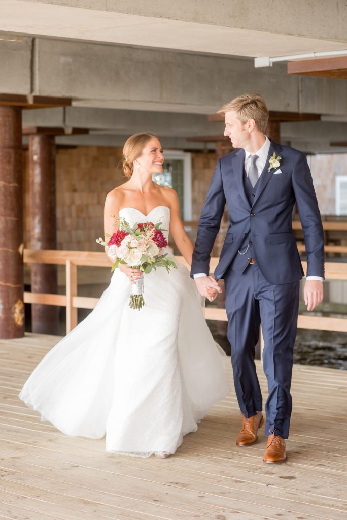 Mikkel Paige Photography photos of a Bay Head Yacht Club nautical wedding. The bride wore a tulle overlay for a second look with her white sweetheart neckline gown and the groom wore a navy blue three-piece suit.