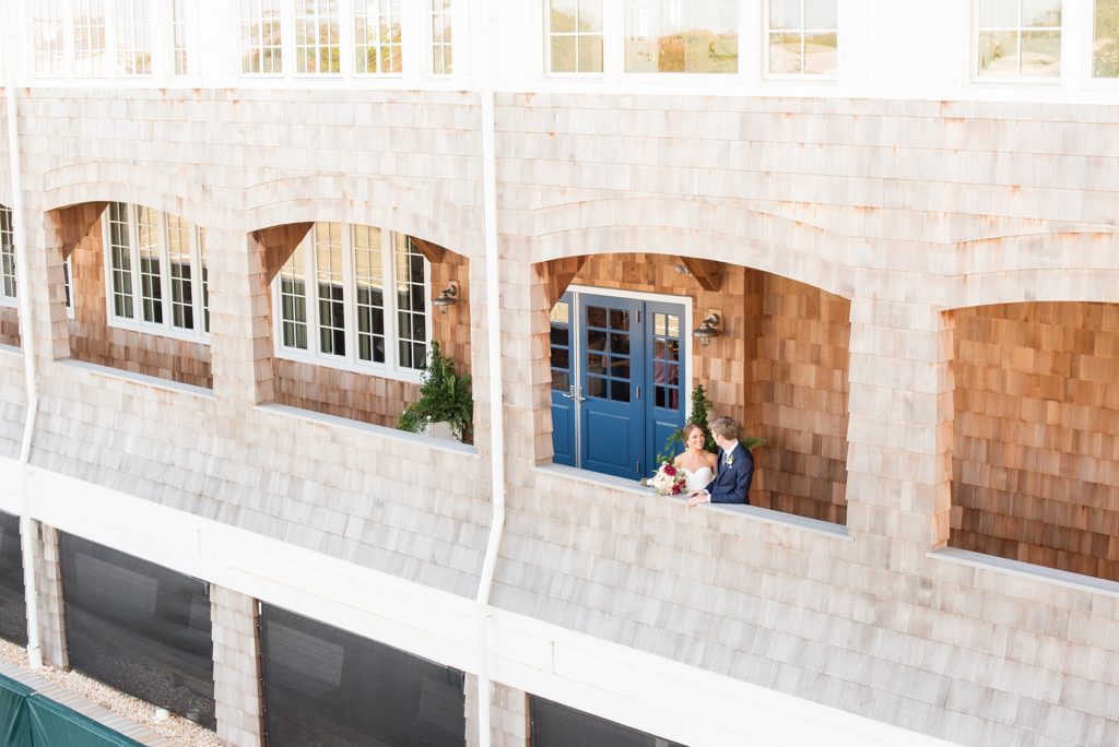 Mikkel Paige Photography photos of a Bay Head Yacht Club nautical wedding. The bride and groom are captured in a wide-view image of the wooden shingle sided waterview venue.