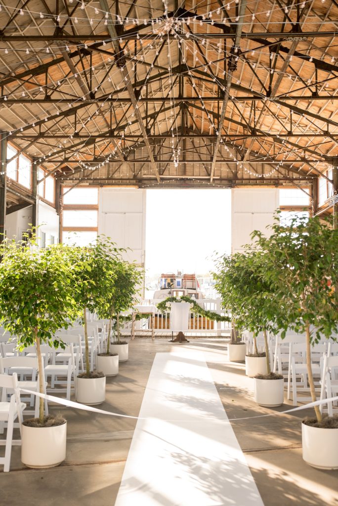 Mikkel Paige Photography picture of a Bay Head Yacht Club nautical wedding. A boathouse ceremony with ficus trees lining the aisle and vintage boat exit.