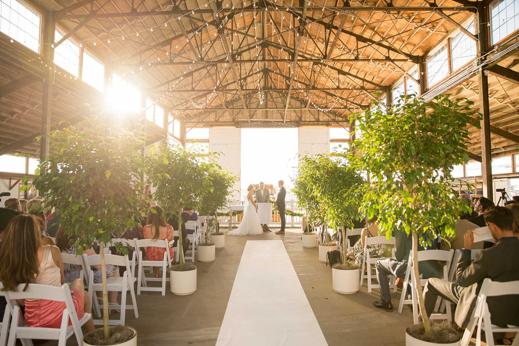 Mikkel Paige Photography picture of a Bay Head Yacht Club nautical wedding. A boathouse ceremony with ficus trees lining the aisle and vintage boat exit.