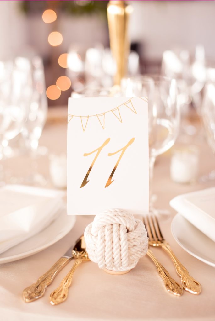 Mikkel Paige Photography picture of a Bay Head Yacht Club nautical wedding. Gold table numbers were help in white rope spheres next to gold flatware.