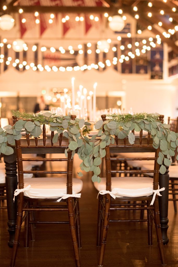 Mikkel Paige Photography picture of a Bay Head Yacht Club nautical wedding. Their bride and groom chairs were decorated with eucalyptus greenery and room lit with bistro lights.