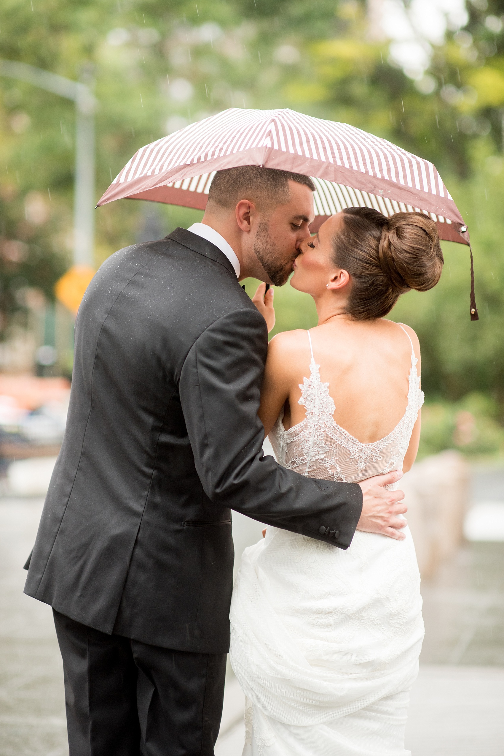 Mikkel Paige Photography photos of a luxury wedding in NYC. First look in Washington Square Park with a picture of the bride and groom under an umbrella kissing in the rain.