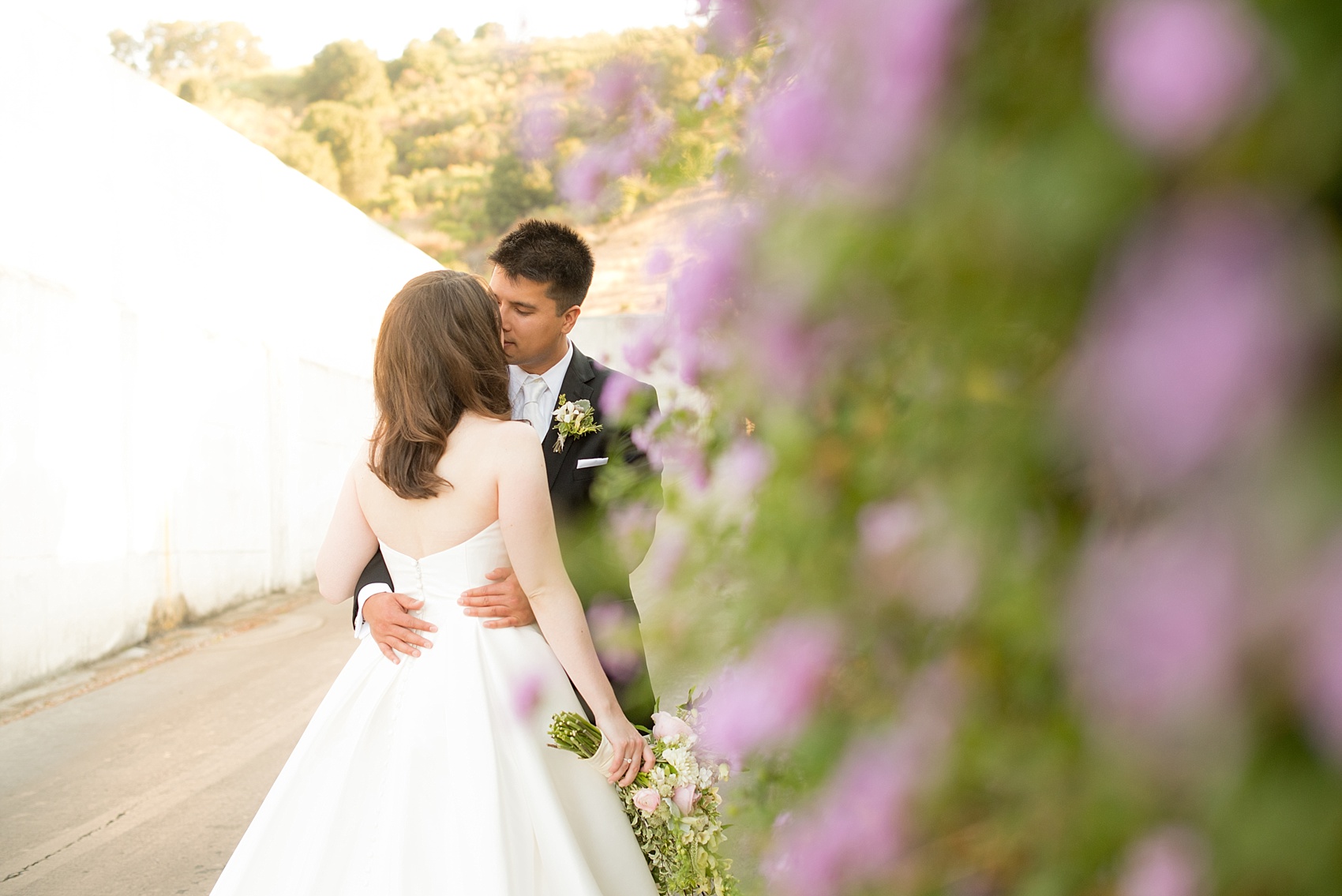 Mikkel Paige Photography kiss photo of the bride and groom at their wedding at Testarossa Winery in Los Gatos, California with a purple flower wall.